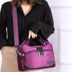 Spacious purple nylon tote bag with decorative charms and black trim, worn with a crossbody strap.