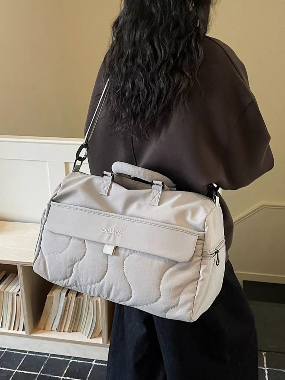 Light grey quilted duffel bag with adjustable strap and top handles.