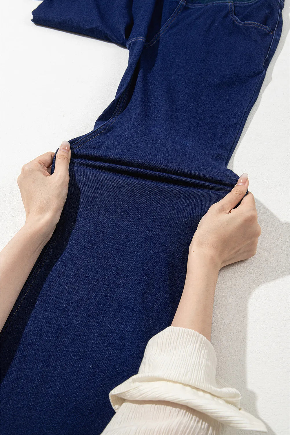 Medium wash denim flare trousers with crossover waist detail shown being stretched.