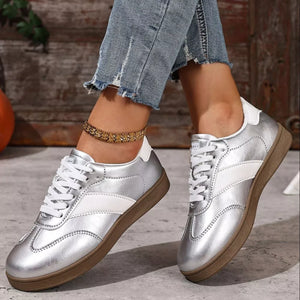 Silver patent leather lace-up sneakers with white accents and brown soles.