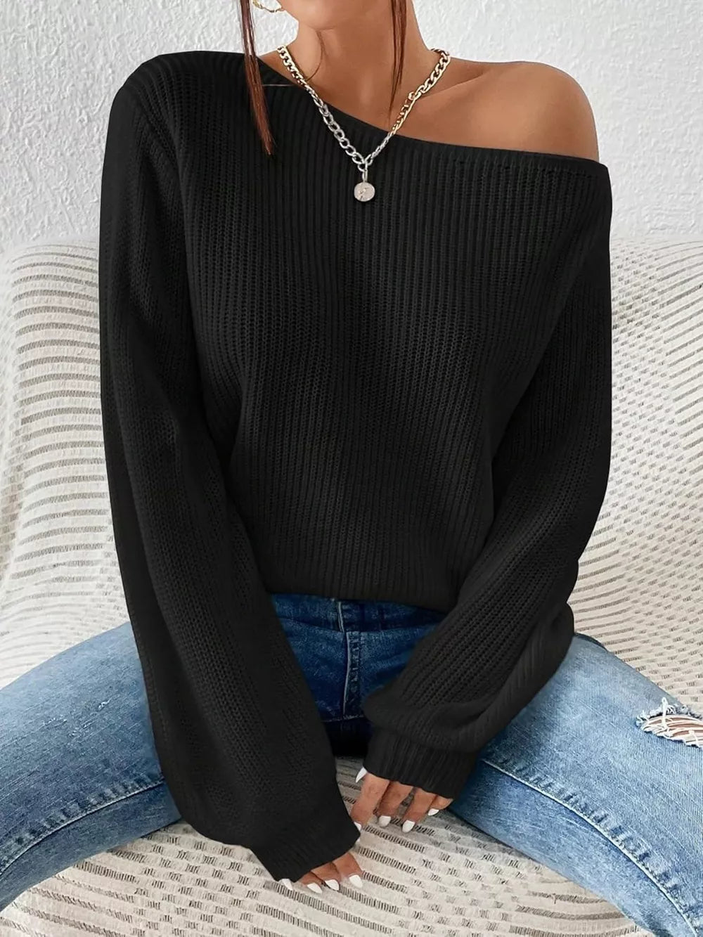 Black asymmetrical knit sweater with off-shoulder neckline and long sleeves.
