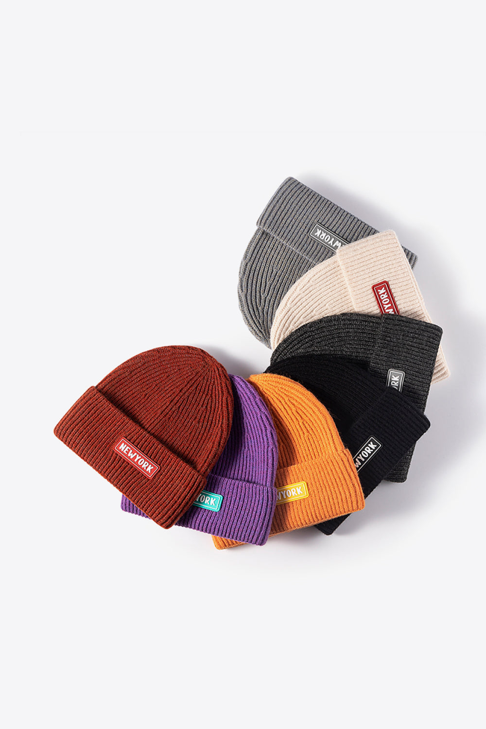 Ribbed acrylic beanies in rust, purple, orange, black, dark gray, beige, and gray, each with a New York patch.