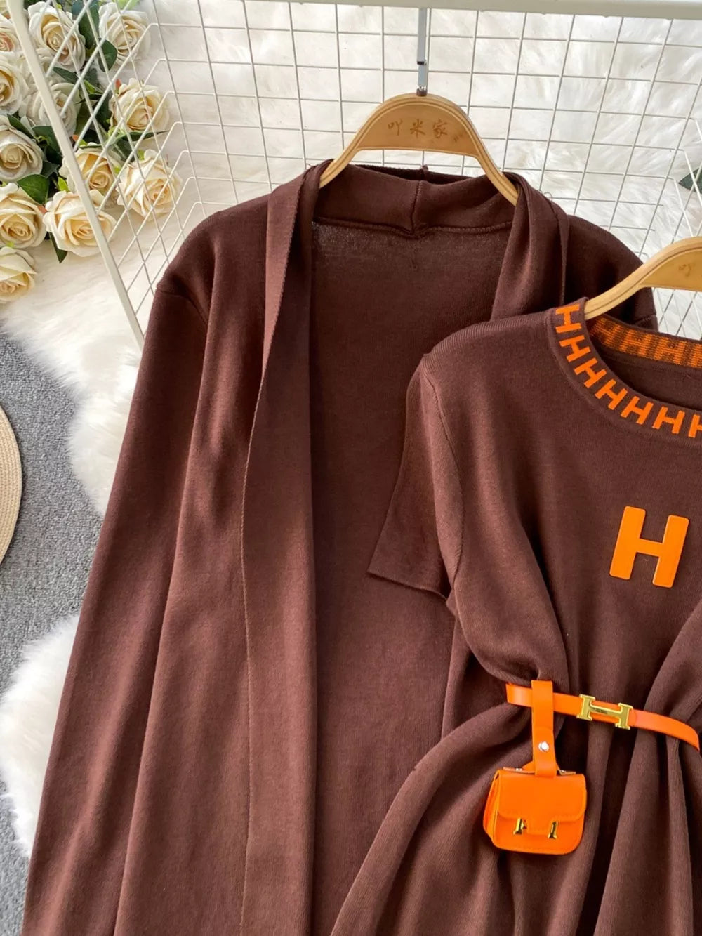 Brown knitted maxi dress and cardigan ensemble with orange belt and mini bag.