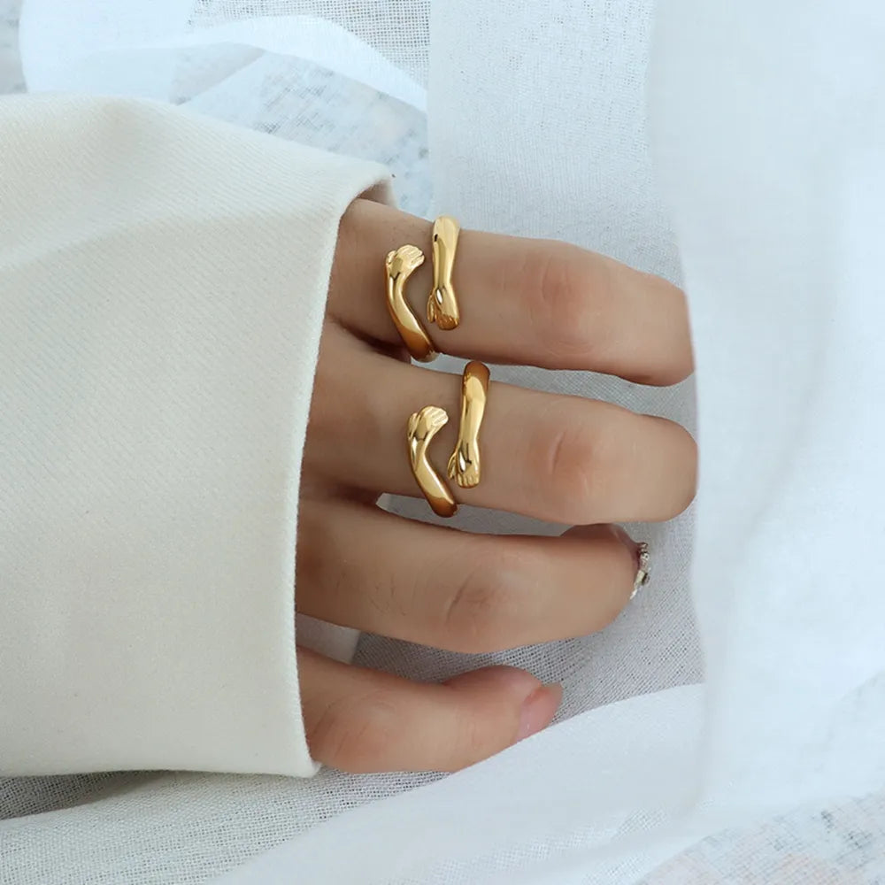 Gold embracing hands open ring on a finger, showing a chic, casual detail.