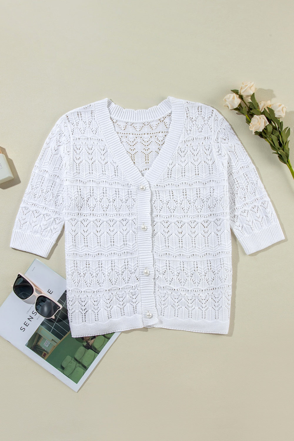 White openwork crochet cardigan with V-neck, pearl buttons, and 3/4 sleeves.