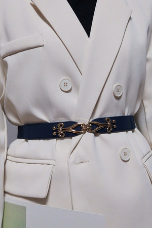 Dark blue elastic belt with ornate gold clasp cinching a cream blazer.