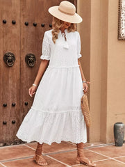 White eyelet midi dress with tie neck, tiered skirt, and ruffled sleeves.