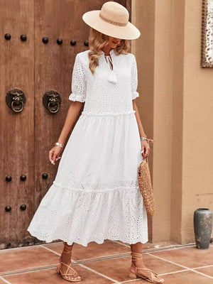 White eyelet midi dress with tie neck, tiered skirt, and ruffled sleeves.