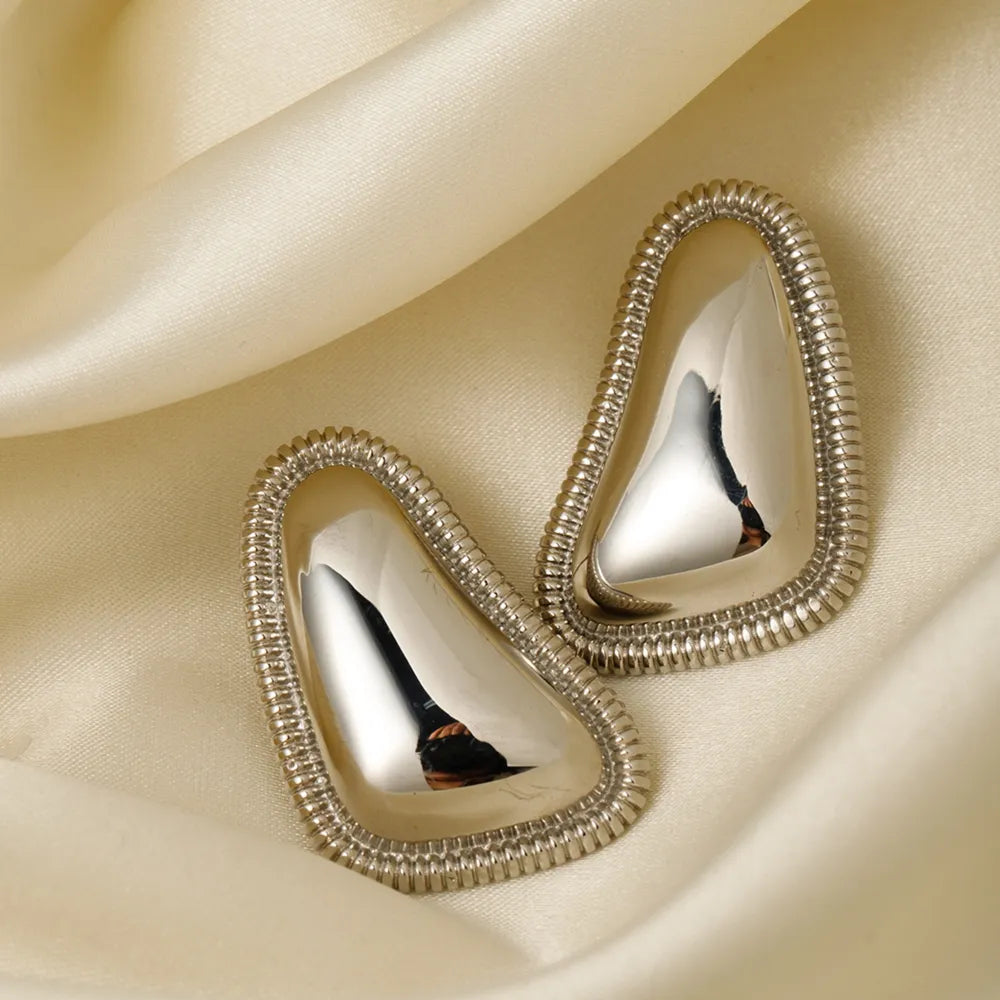 Sculpted silver vermeil earrings with textured edges on satin fabric