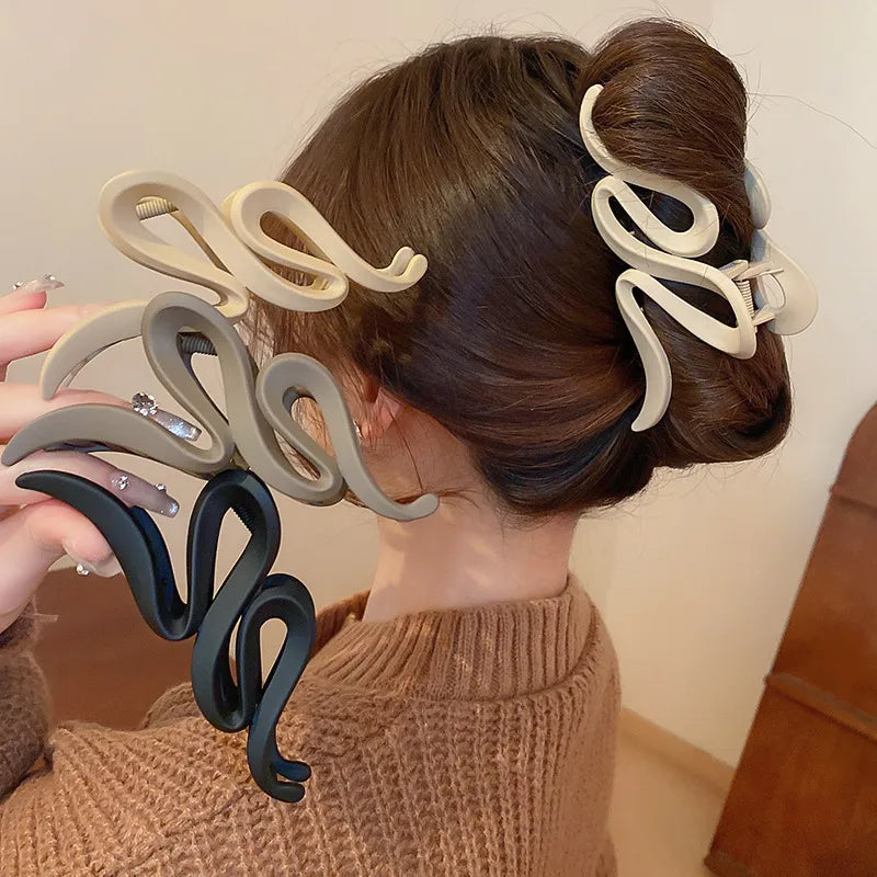 Sculptural hair claw clips in black, tan, and dust storm acrylic with serpentine design.