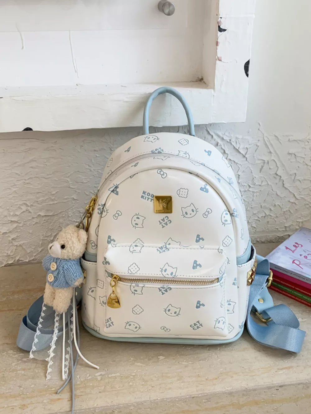 White backpack with blue cat pattern and teddy bear charm
