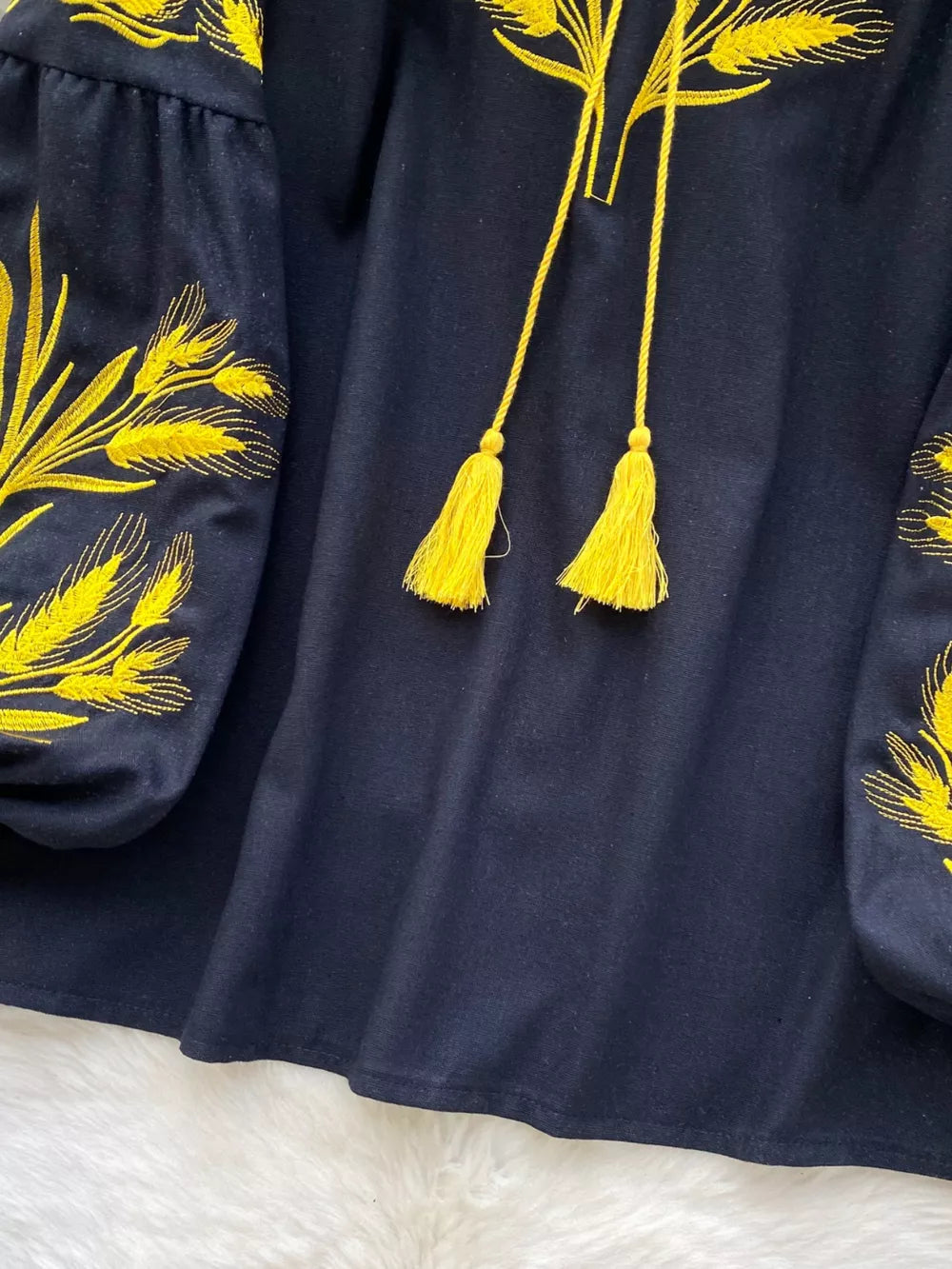 Black tie-neck blouse with yellow wheat embroidery on sleeves and yellow tassels.