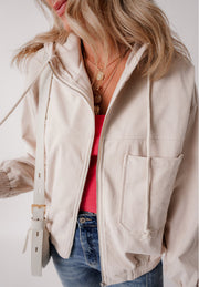 Cream corduroy bomber hoodie with zip front, drawstring hood, and chest pocket.