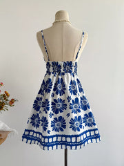 White mini dress with blue floral print, smocked waist, and spaghetti straps.