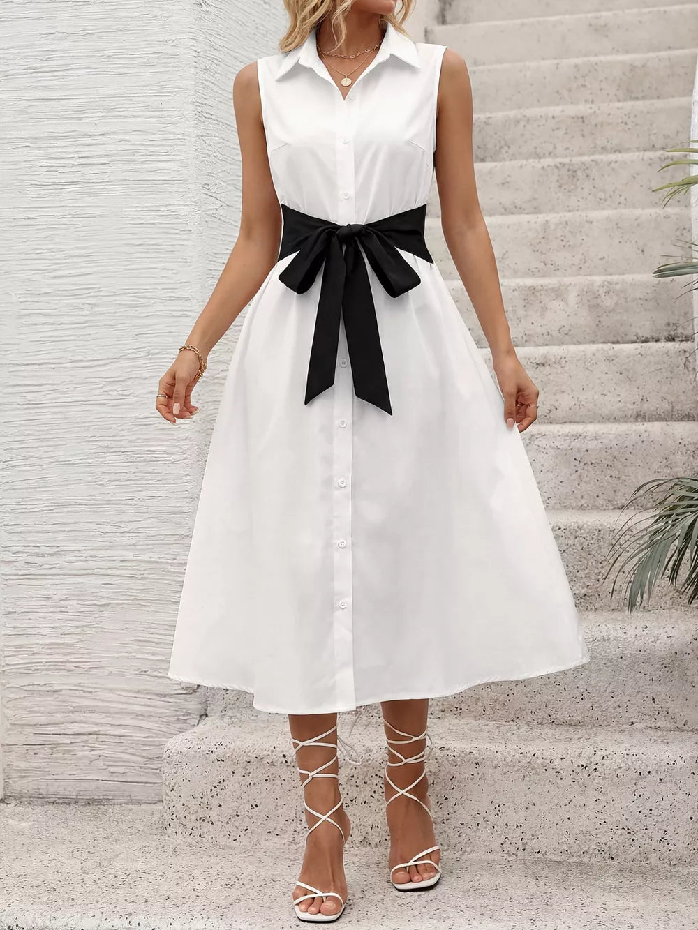 White midi shirt dress with black bow tie belt, button front, and sleeveless design.