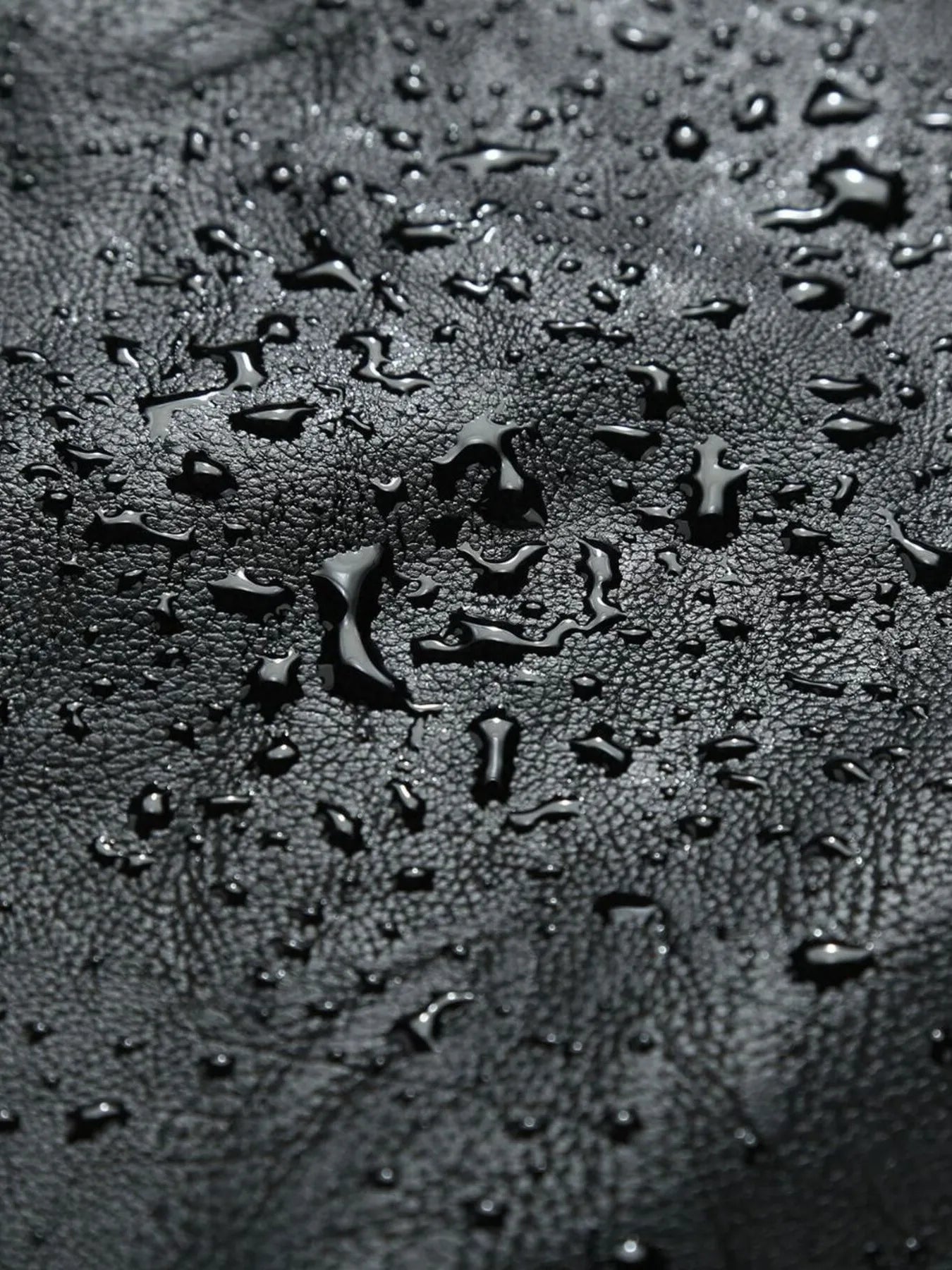 Black moto jacket material with water droplets, showing texture.
