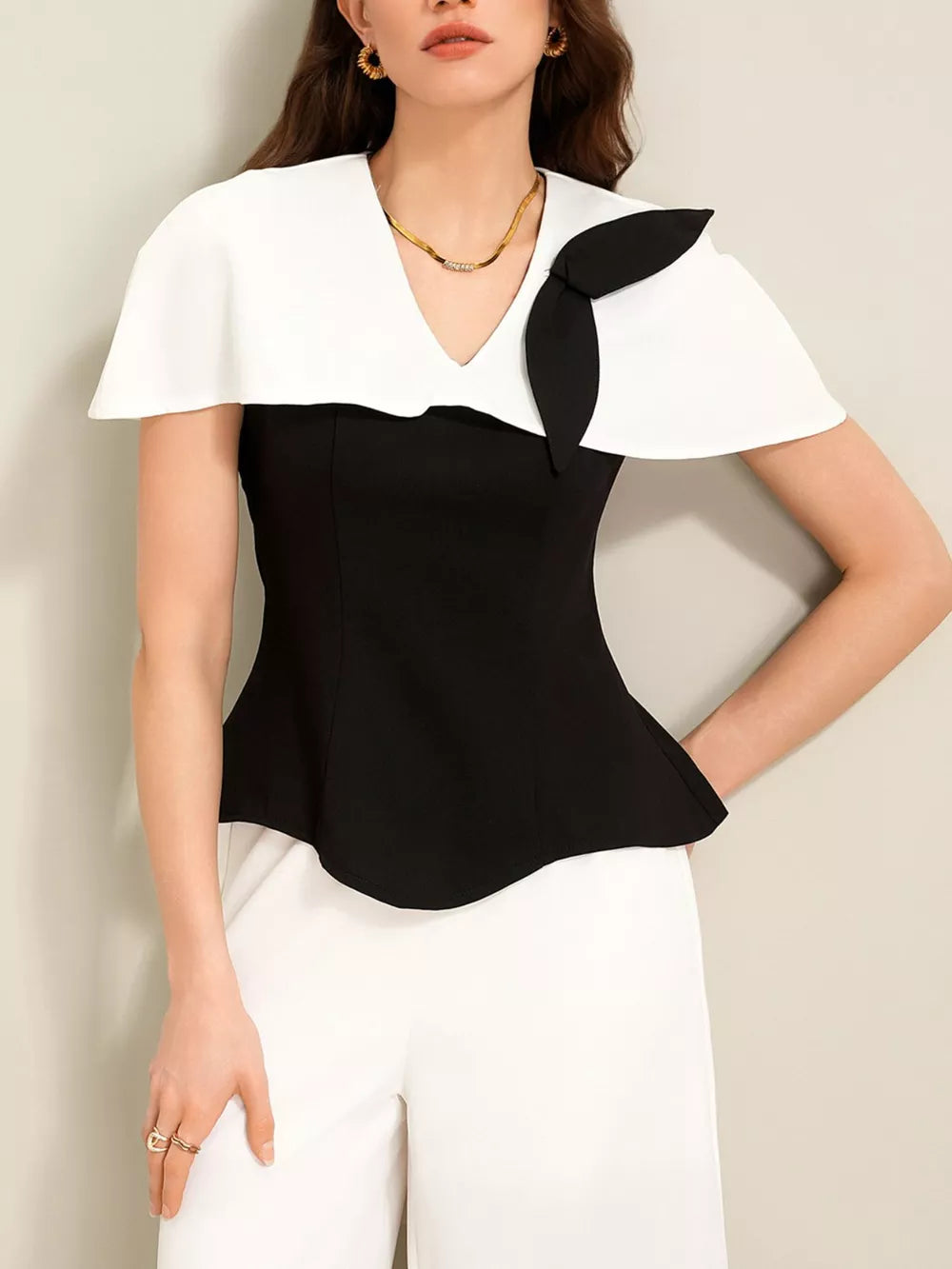 Black peplum top with white cape collar and bow detail, paired with white wide-leg pants.