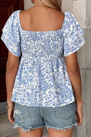 White and blue floral babydoll shirt with smocked bodice and ruffled sleeves.