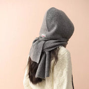 Gray hooded knit scarf with tie detail and ribbed texture, worn over a cream sweater.