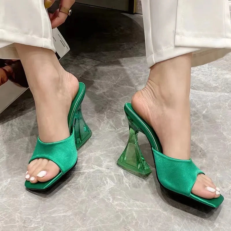 Dark green satin mules with a sculpted clear heel and square toe.