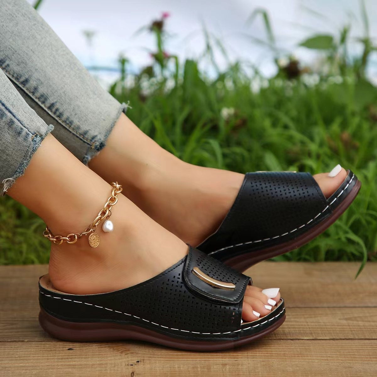 Black perforated wedge sandals with gold accent and white stitching.