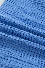 Blue midi dress with a subtle checkered texture and crinkled fabric detail.