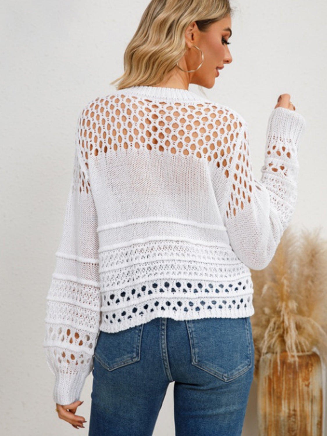 White openwork knit sweater with textured details and long sleeves.