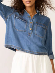 Blue denim cropped half snap shirt with two chest pockets and gold buttons.