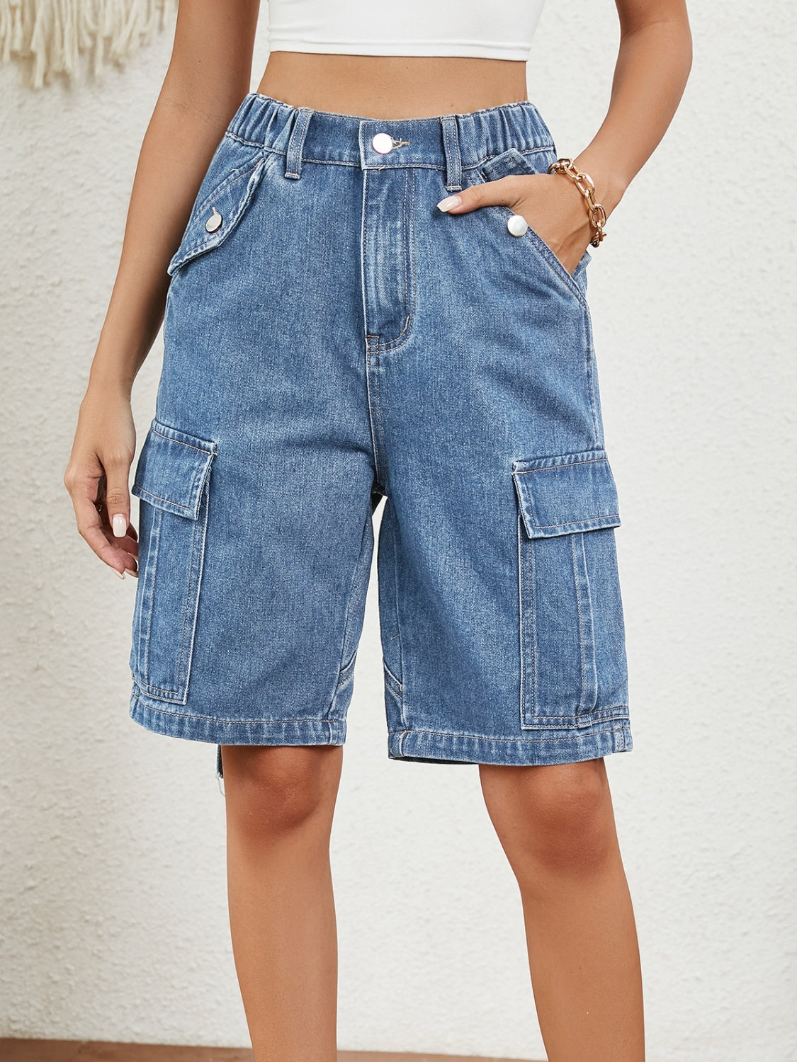 Denim cargo bermuda shorts in medium wash with buttoned pockets and elastic waist.