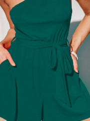 Dark green asymmetrical knot-waist romper with one-shoulder neckline and side pockets.