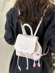 White leather mini drawstring backpack with beaded details and a fuzzy pink charm.