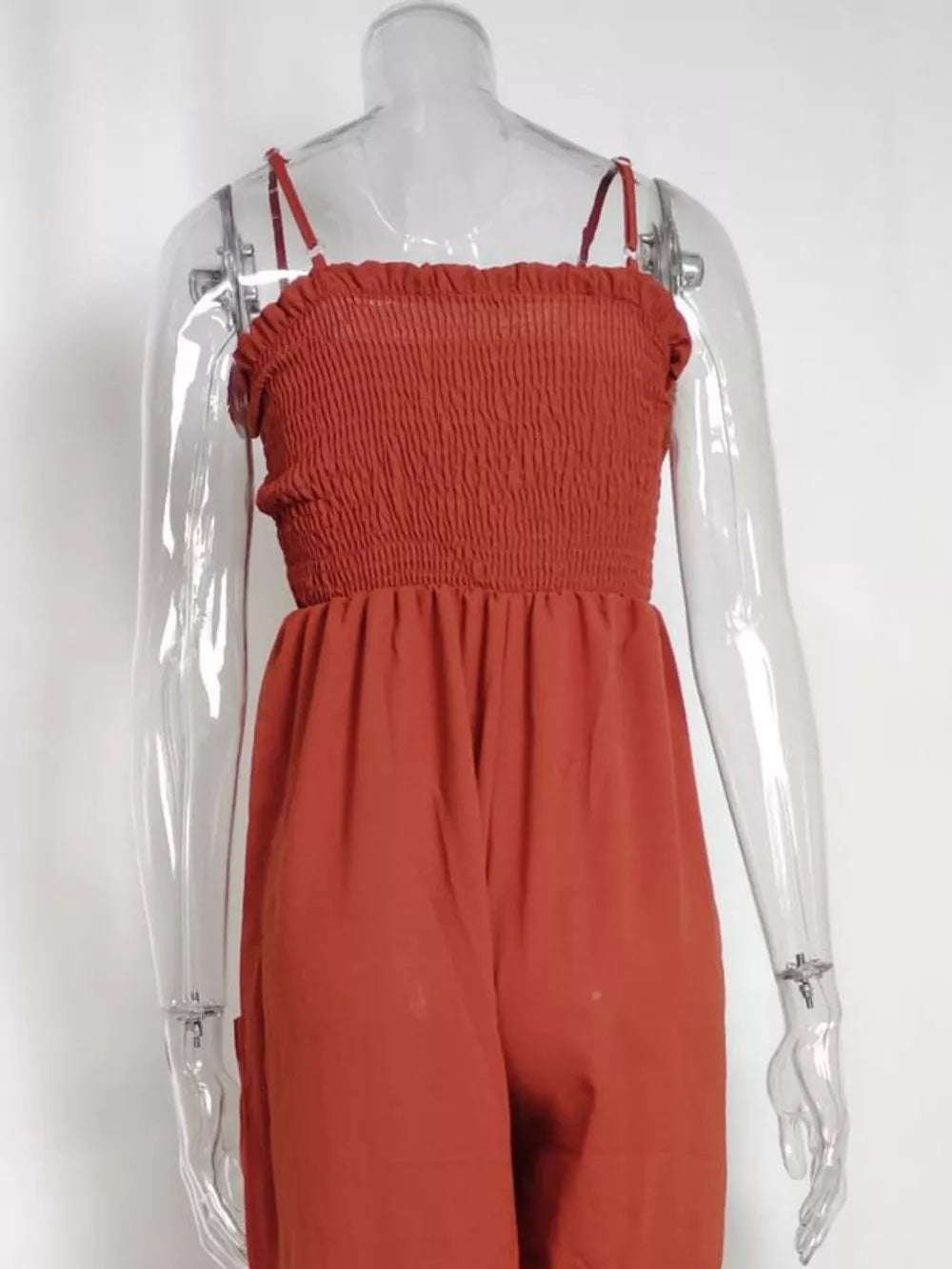 Orange-red smocked wide leg romper with spaghetti straps and pockets.