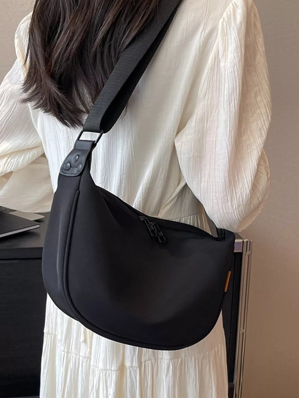 Black crescent-shaped crossbody bag with adjustable strap and zipper closure.