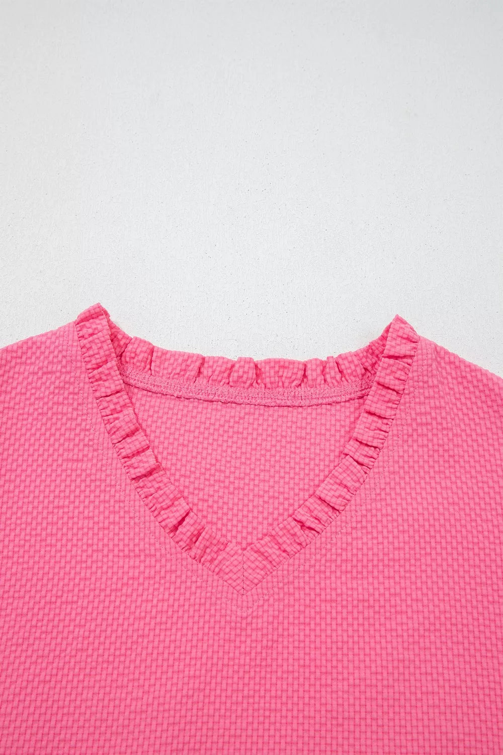 Women's pink textured V-neck blouse with ruffled neckline detail