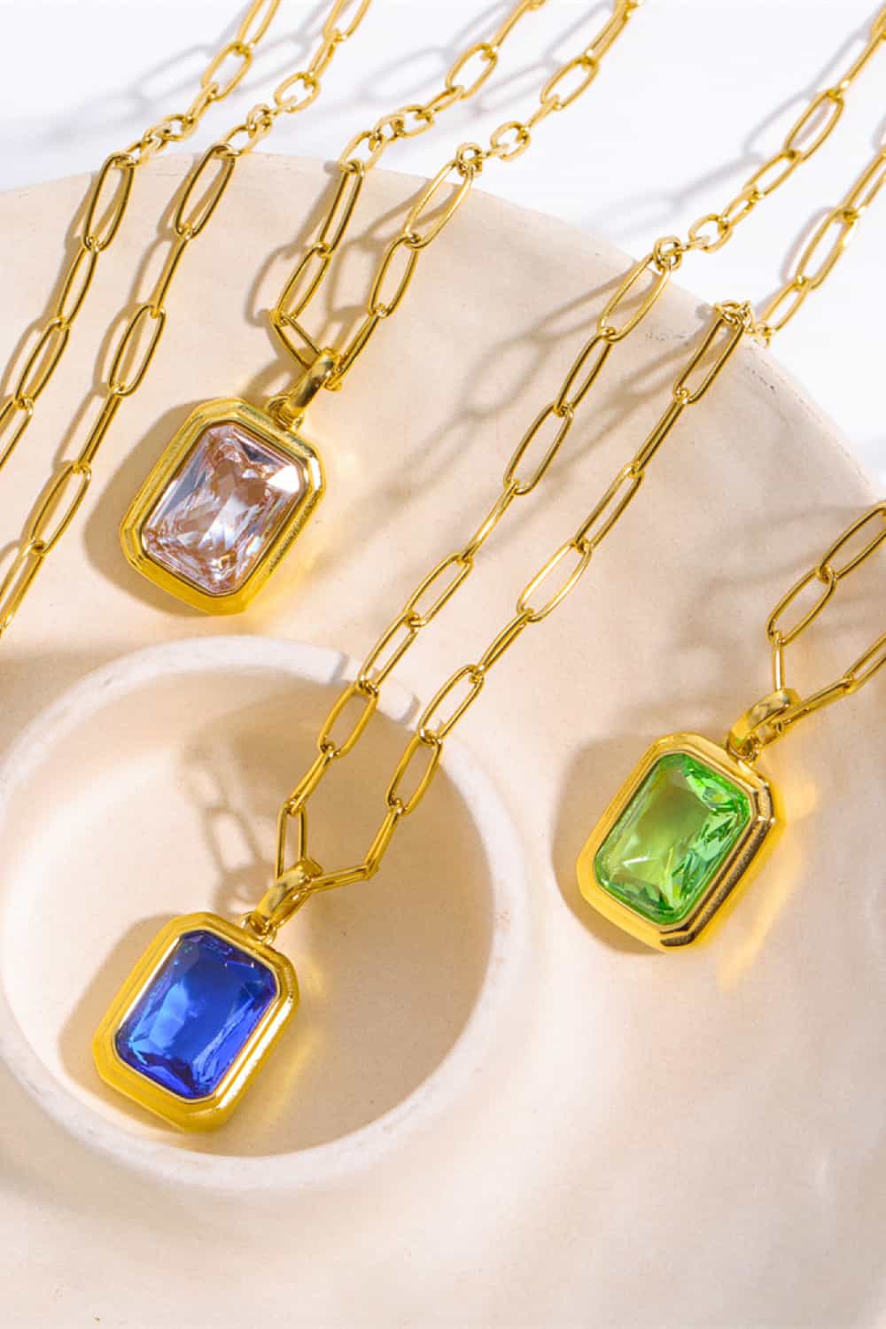 Gilded Prism Pendant Necklace with royal blue, transparent, and light green gemstones on a gold chain.