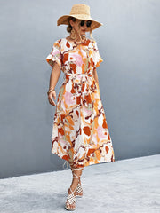 Women's abstract print midi dress with tie waist, short sleeves, and A-line cut in orange-red and blue tones.