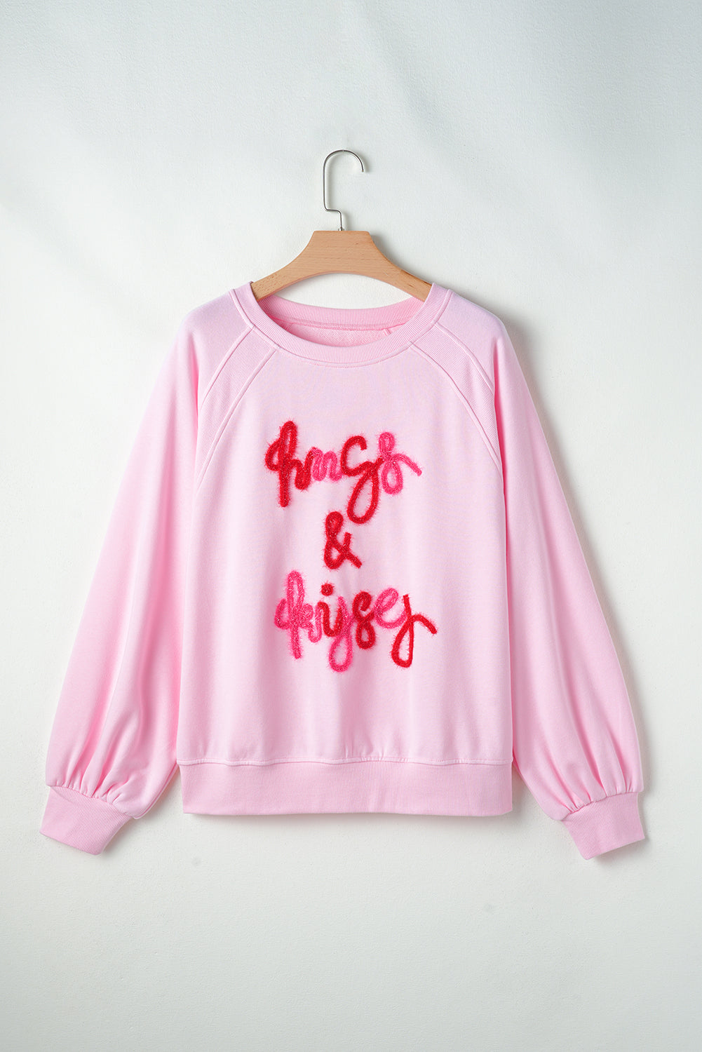 Blush pink sweatshirt with embroidered "hugs & kisses" graphic and balloon sleeves.