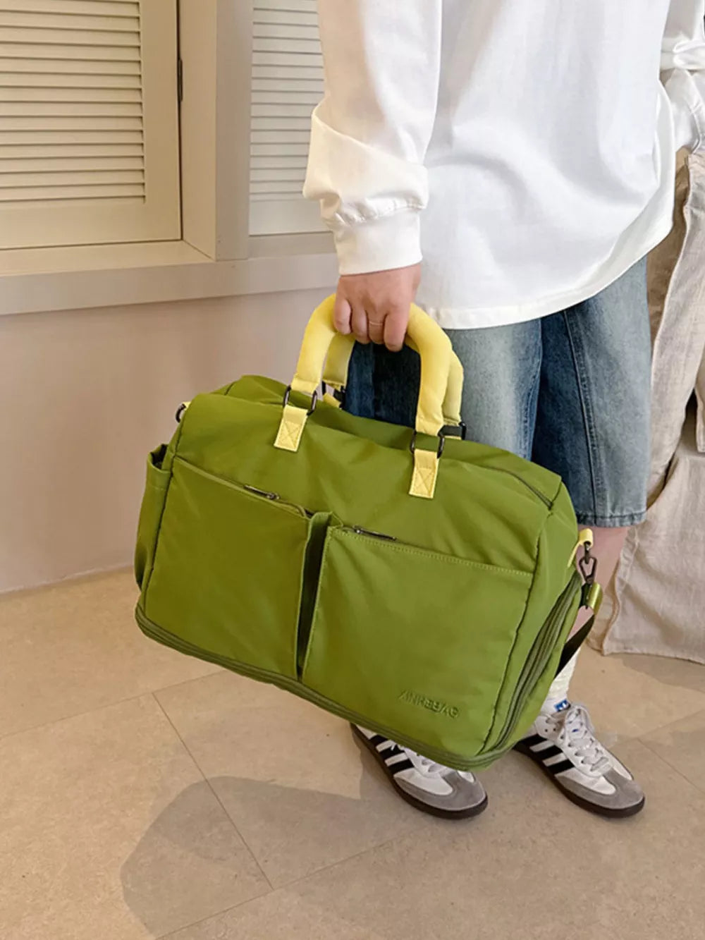 Green travel bag with yellow handles and multiple front pockets, adjustable strap.
