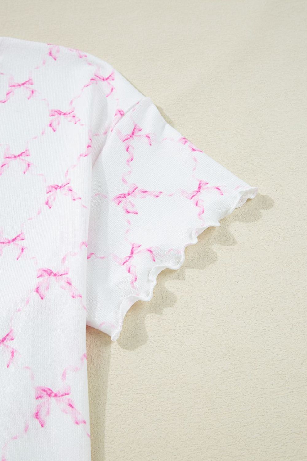White loungewear top with pink bow print and scalloped lettuce edge sleeves.