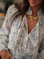White long-sleeve blouse with blue floral print, tie neck, and ruffled cuffs.