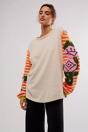 Beige long sleeve tee with embroidered floral detail on orange striped sleeves.