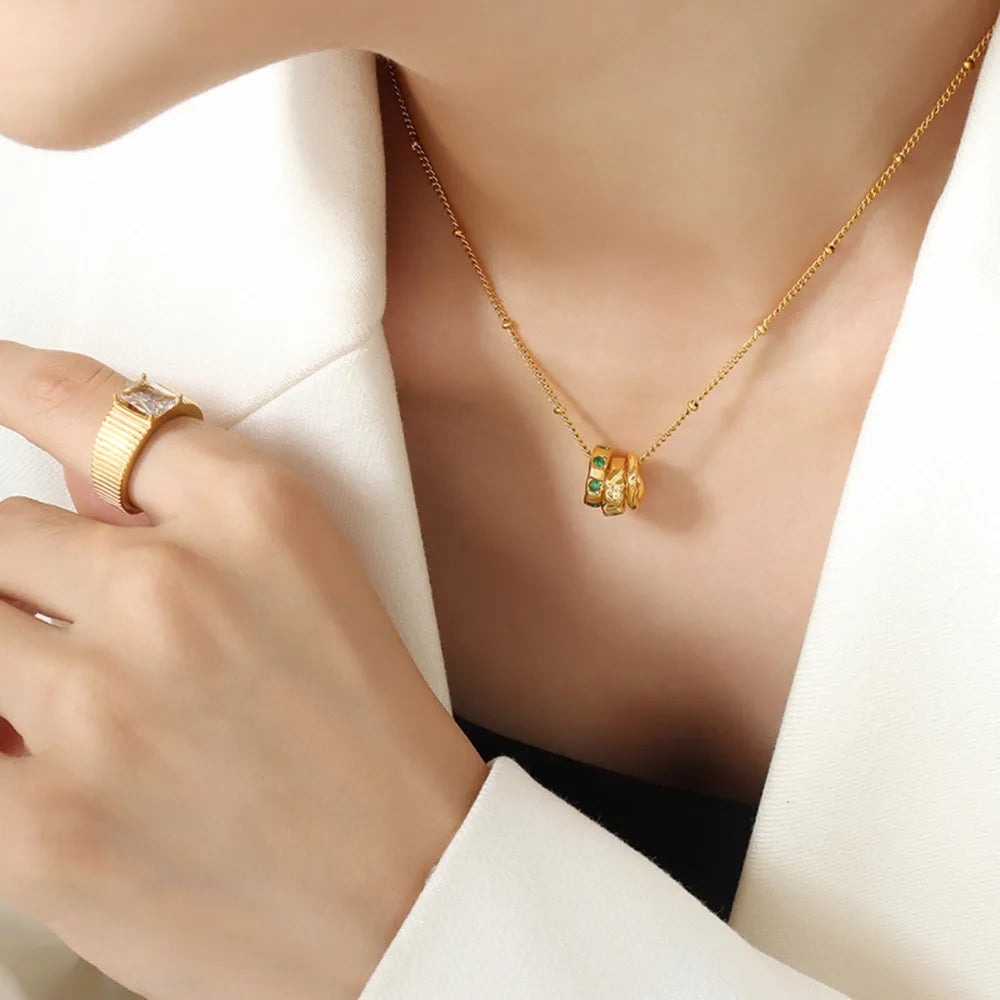 Gold necklace with interlocking circles featuring emerald stones and a beaded chain.