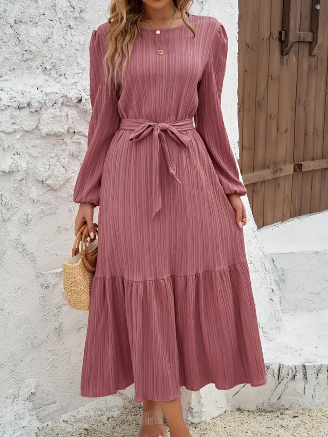 Pink pleated midi dress with tie waist, long sleeves, and tiered hem.