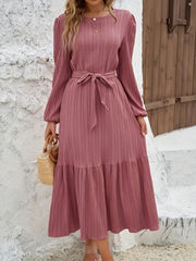 Pink pleated midi dress with tie waist, long sleeves, and tiered hem.
