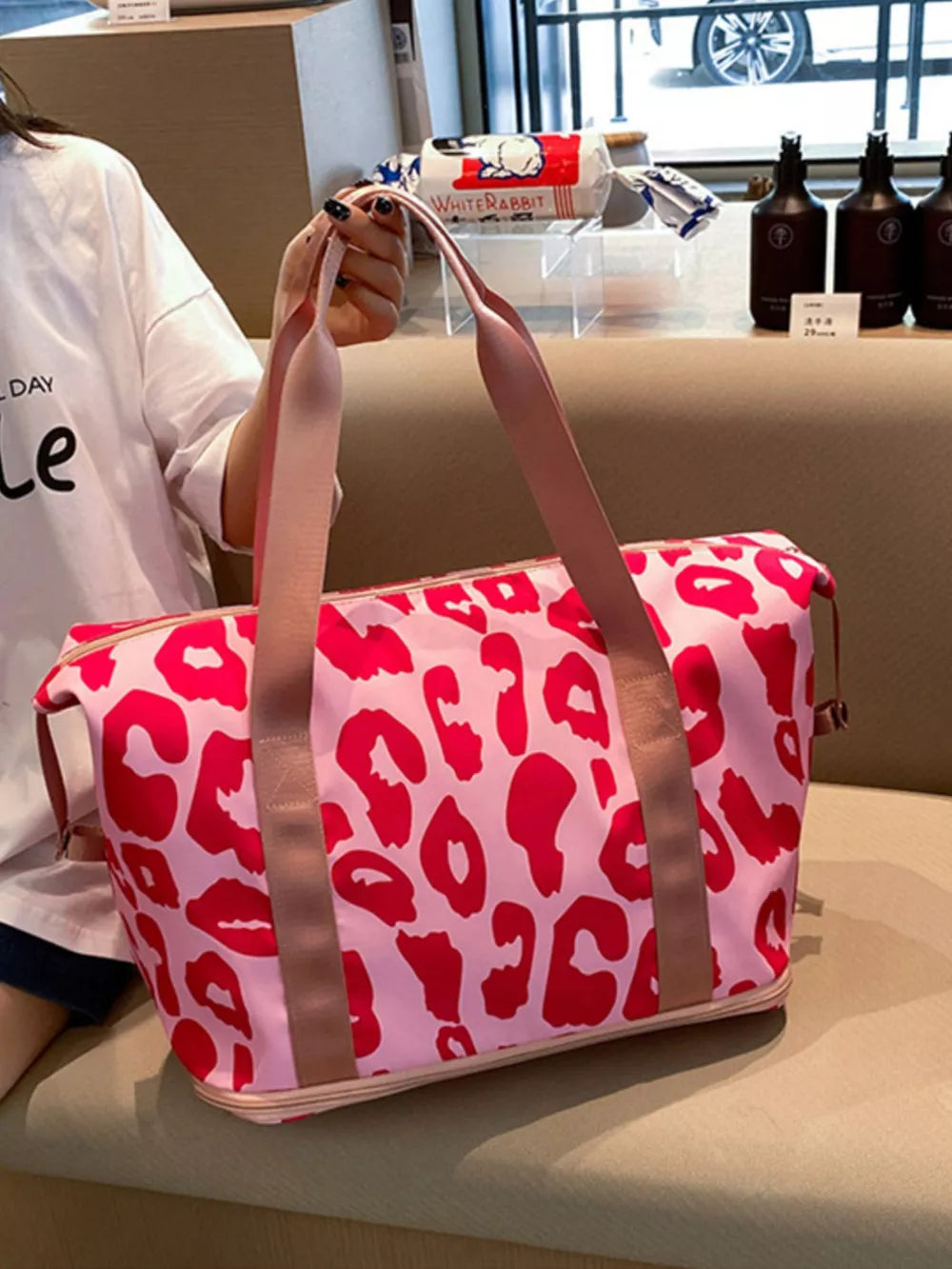 Vibrant leopard print travel bag with pink and red pattern, dual pink straps, and tan trim.