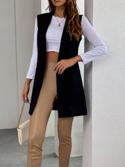 Black draped lapel vest with asymmetric hemline, worn over a white crop top and tan pants.