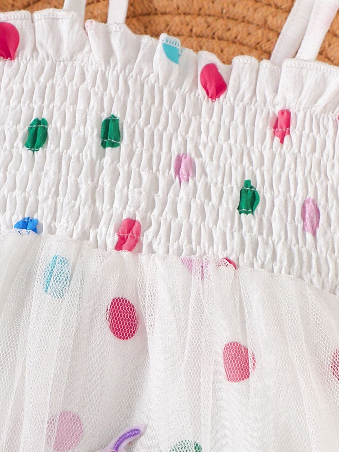 White smocked bodysuit dress with colorful polka dot ribbon details and tulle skirt.