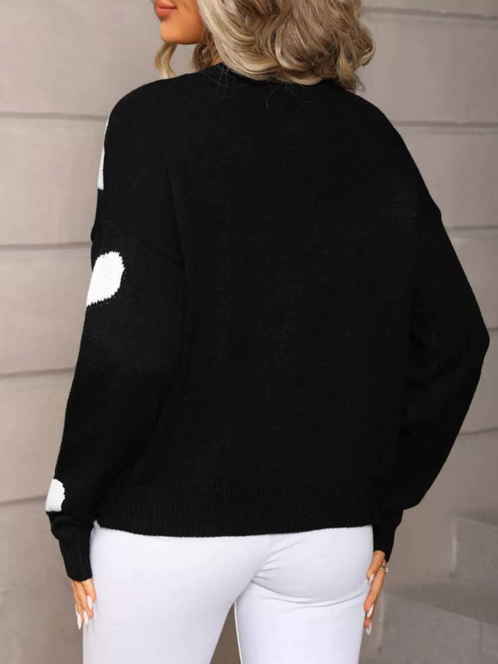 Black knit cardigan with white heart pattern, button-up front, crew neck, long sleeves.
