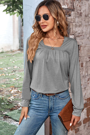 Grey long sleeve top with square neckline and subtle pleats, styled with jeans.