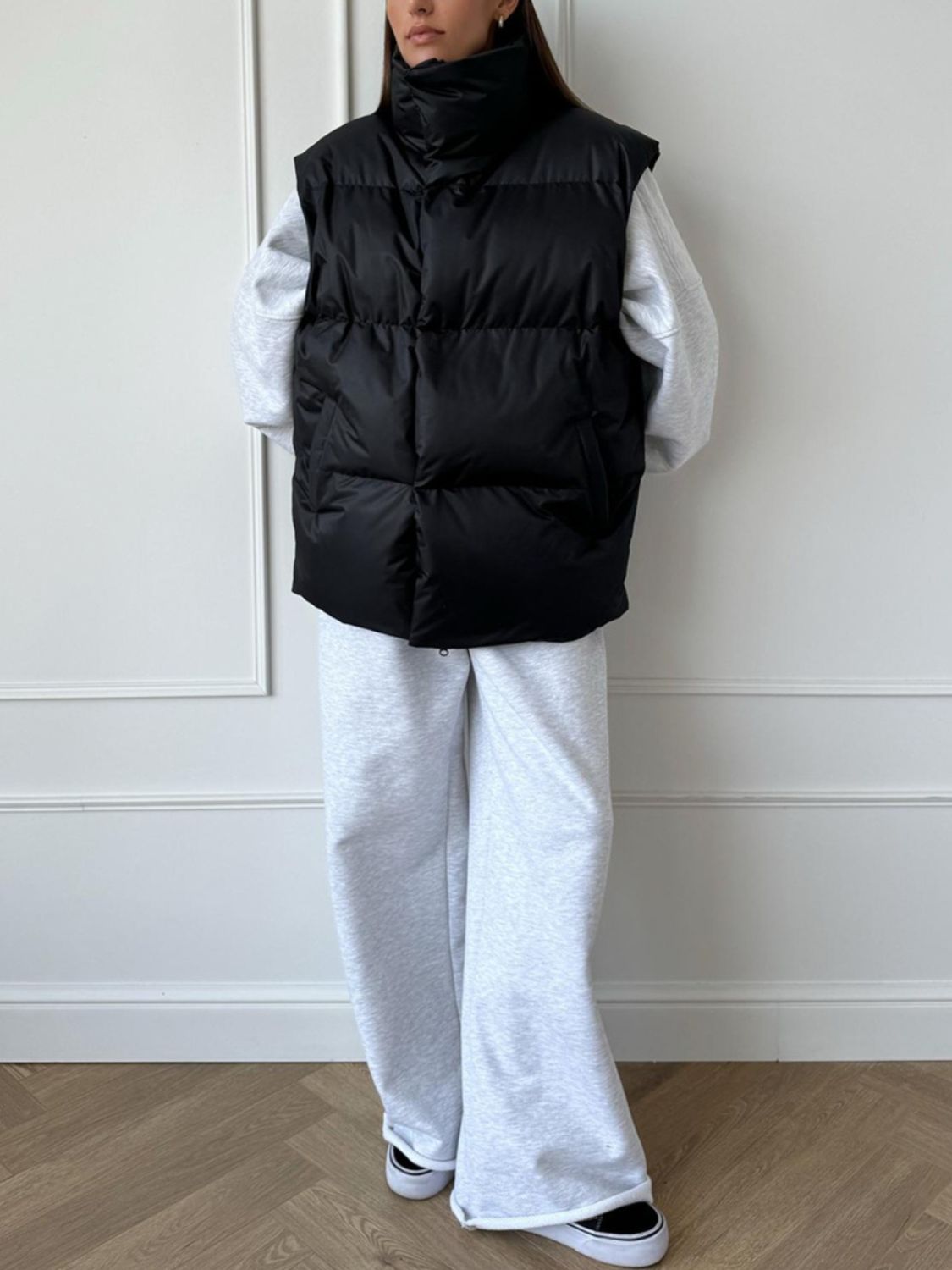 Black padded puffer vest with a high collar, worn over a grey sweatshirt and light grey sweatpants.